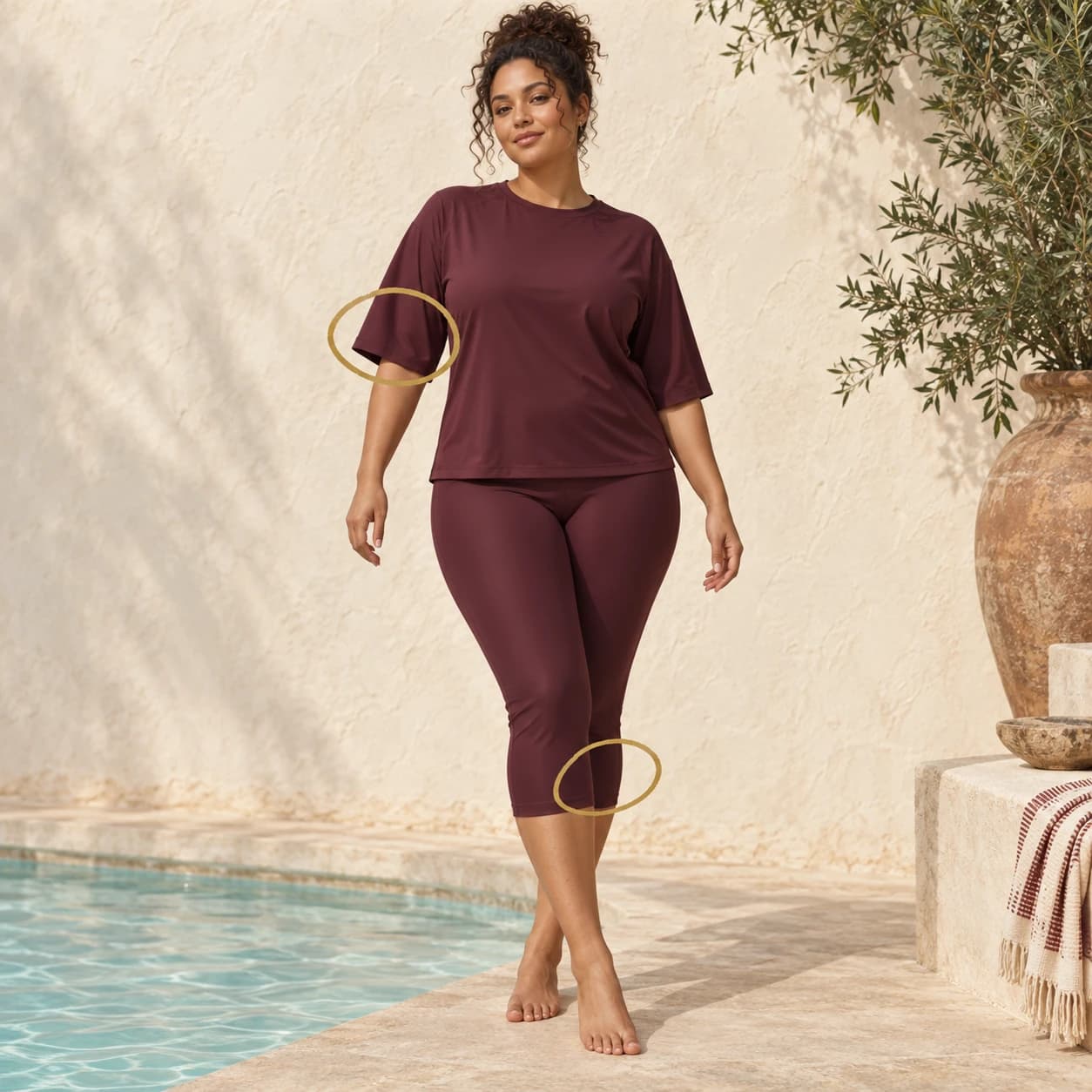 A woman in an oxblood elbow-sleeve swim top and capri swim pants; brass circles highlight both hems.